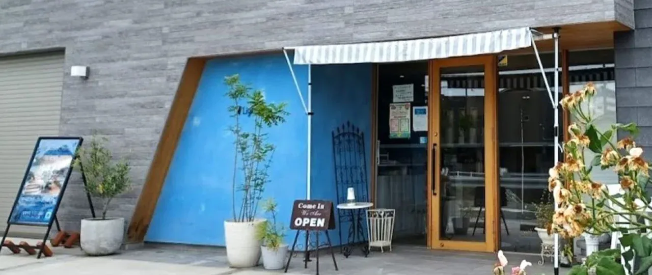 カフェ ライトブルー の外観。水色のファサードに木の扉、OPEN の看板を置いた入口